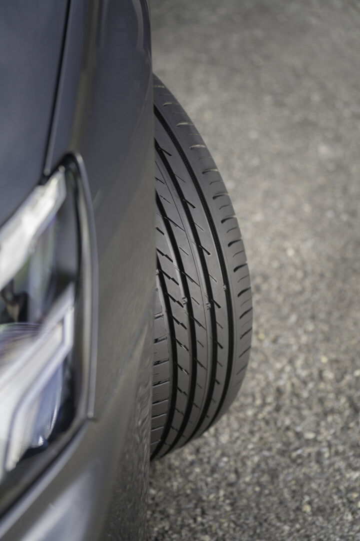 Vue rapprochée en biais d’un pneu monté sur une voiture, montrant quatre rainures longitudinales et des nervures centrales à entailles obliques.